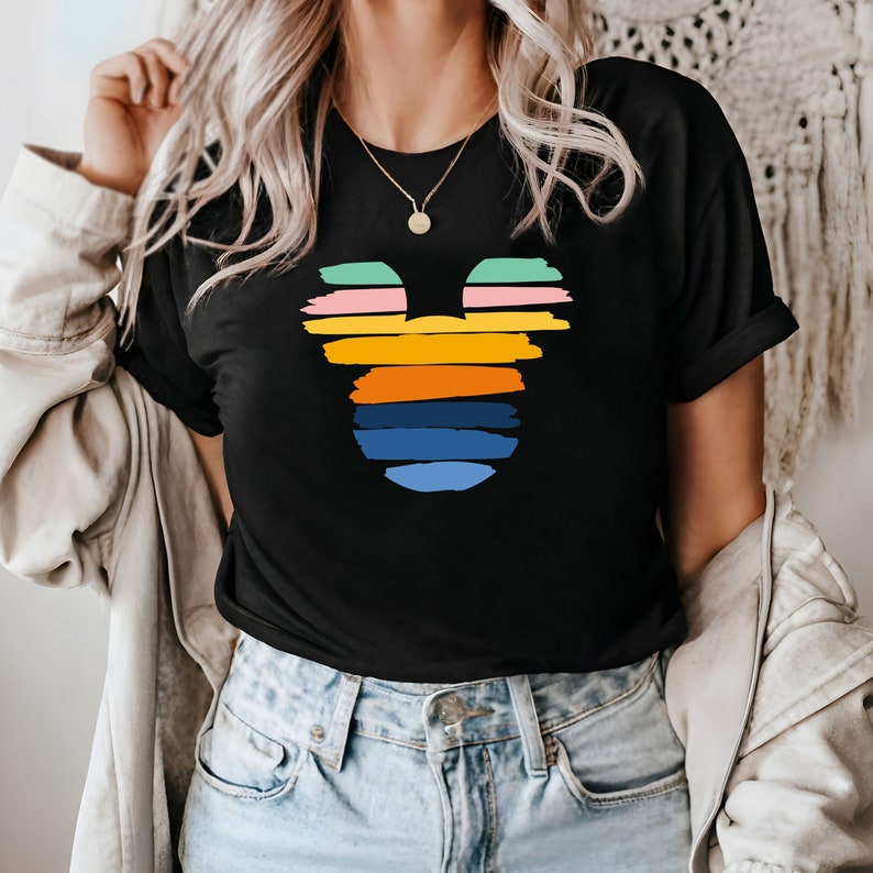 May include: A black t-shirt with a colorful Mickey Mouse silhouette design. The silhouette is made up of horizontal stripes in shades of pink, orange, yellow, green, and blue.