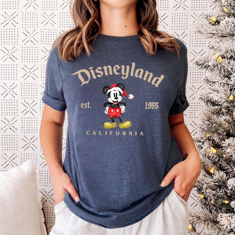 May include: A navy blue t-shirt with a vintage Disneyland logo featuring Mickey Mouse wearing a Santa hat. The text reads "Disneyland est. 1955 California".
