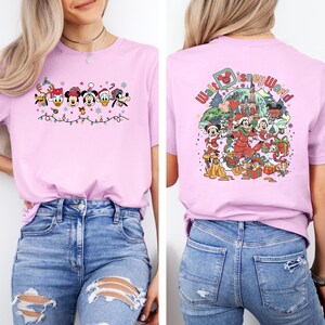 Op de afbeelding: Lichtroze T-shirt met een feestelijk Disney-ontwerp. De voorkant toont Disney-personages in feestelijke kleding met lichtslingers. De achterkant heeft een "Walt Disney World"-afbeelding met personages en cadeaus, perfect voor Disney-fans.