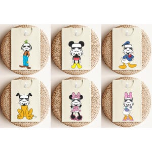 May include: Six beige t-shirts featuring cartoon characters with Stormtrooper helmets. Characters include Goofy, Mickey Mouse, Donald Duck, Pluto, Minnie Mouse, and Daisy Duck. Each shirt is displayed on a round, woven placemat.