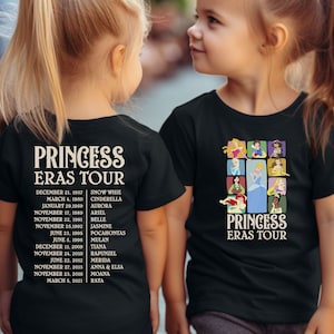 以下が含まれることがあります： プリンセスをテーマにした黒いTシャツを着た子供2人。Tシャツには、ディズニーのプリンセスのコラージュと「プリンセス・エラス・ツアー」の文字が書かれている。左側のTシャツの文字は、プリンセスの映画公開順に並んでいる。