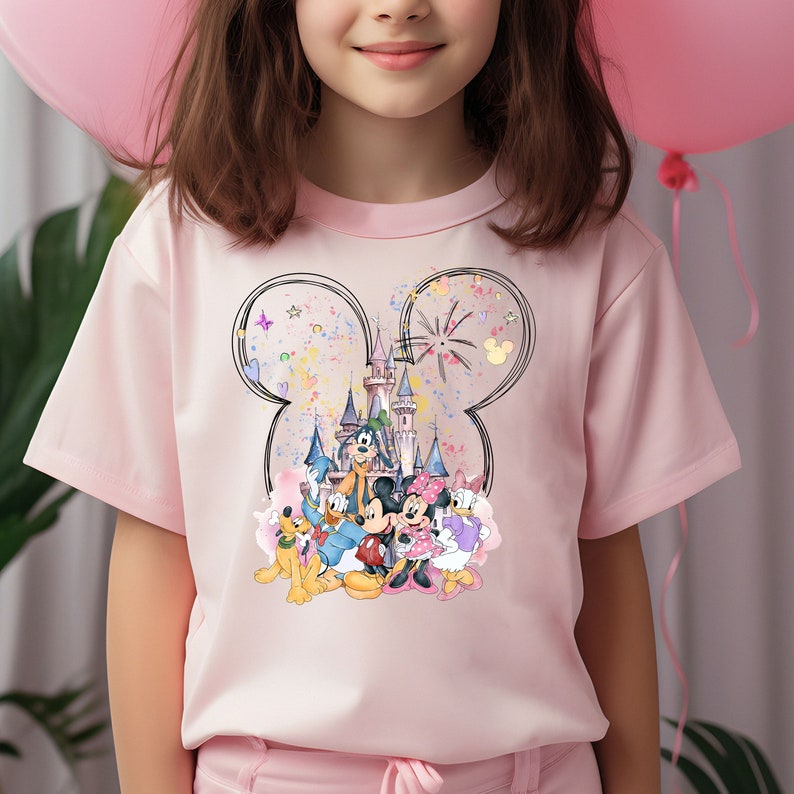May include: Pink t-shirt with a graphic of Mickey Mouse and friends in front of the Disney castle. The graphic is surrounded by confetti and fireworks. The graphic is in the shape of Mickey Mouse's ears.