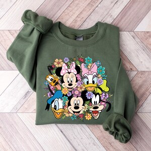 May include: A green sweatshirt with a colorful graphic print of Mickey Mouse, Minnie Mouse, Donald Duck, Goofy, and Pluto surrounded by flowers.