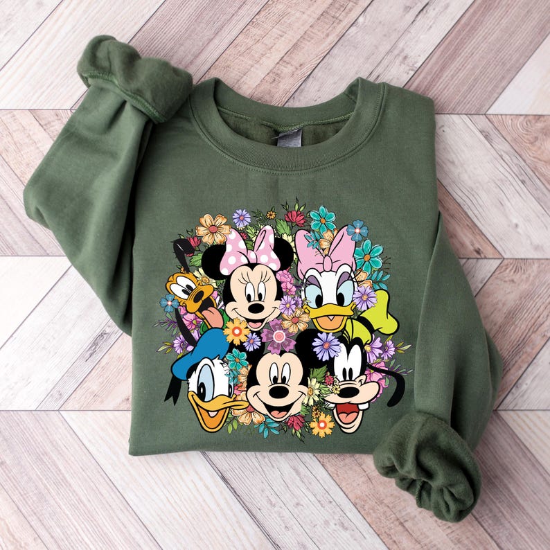 May include: A green sweatshirt with a colorful graphic print of Mickey Mouse, Minnie Mouse, Donald Duck, Goofy, and Pluto surrounded by flowers.