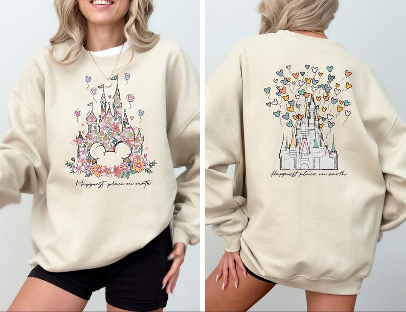 May include: A beige sweatshirt with a graphic of a floral castle and the text "Happiest place on earth". The castle is surrounded by colorful balloons in the shape of hearts.