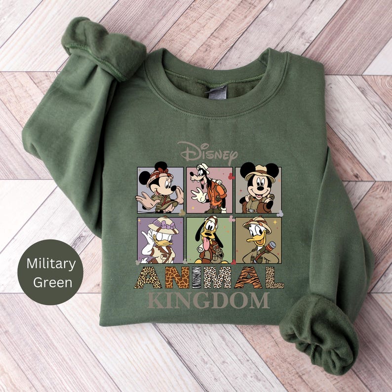 May include: A green sweatshirt with a graphic of Mickey Mouse, Goofy, Donald Duck, and Pluto dressed as safari explorers. The graphic includes the text "Disney Animal Kingdom".