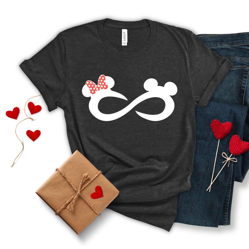 May include: A dark grey t-shirt with a white infinity symbol design. The infinity symbol has a red and white polka dot bow on one side and a mouse ear on the other side.