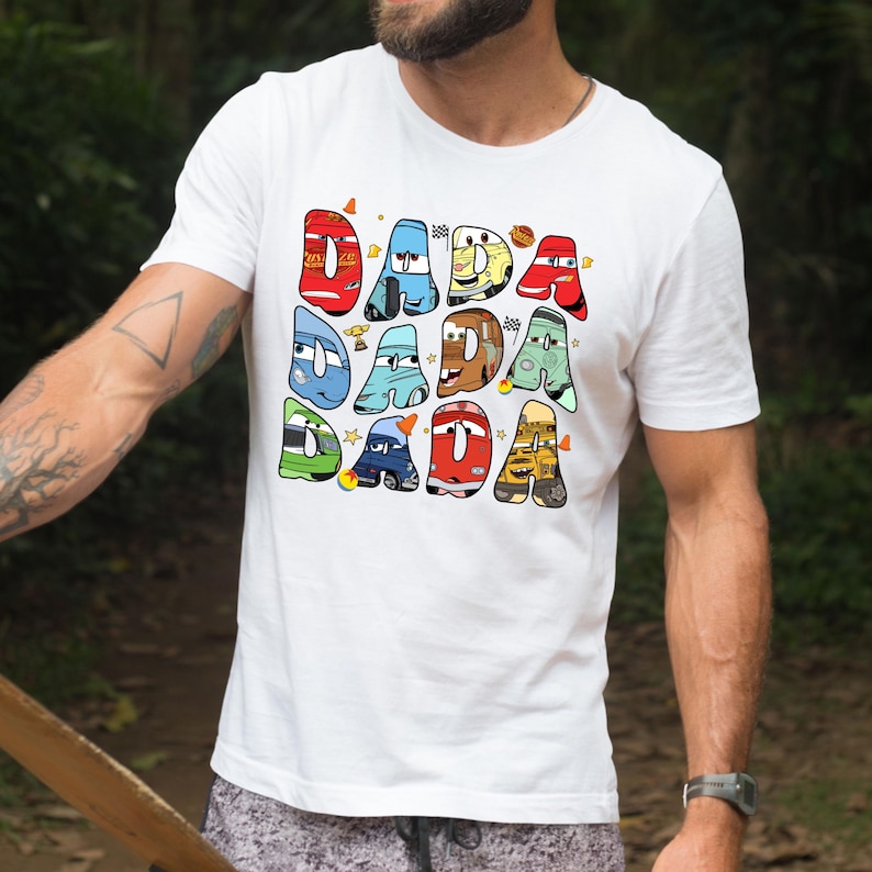 May include: White t-shirt with a colorful graphic of the word "DADA" spelled out with cartoon cars from the movie Cars.