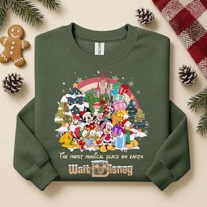 Op de afbeelding: Donkergroene sweatshirt met een afbeelding van Disney-personages, kerstbomen en een regenboog. De tekst luidt "The most magical place on earth" en "Walt Disney". Een feestelijk sweatshirt met een vakantiethema.