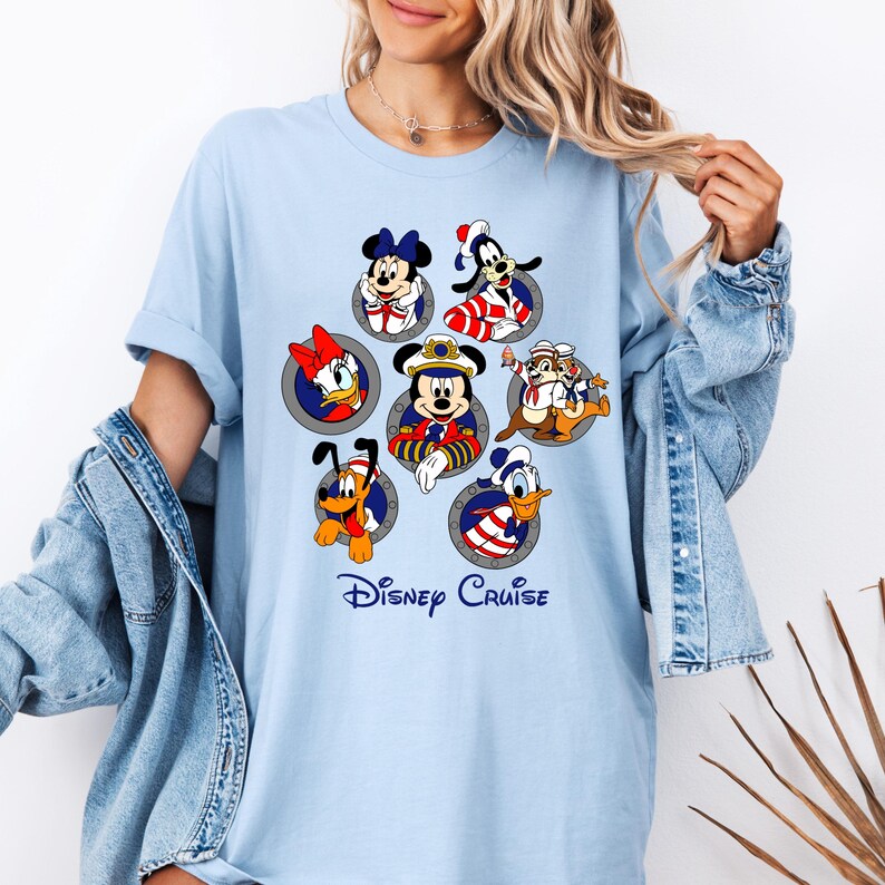 May include: Light blue t-shirt featuring Disney characters in porthole designs. Characters include Mickey Mouse, Minnie Mouse, Donald Duck, Goofy, Pluto, Daisy Duck, Chip and Dale. The words "Disney Cruise" are printed below the characters.