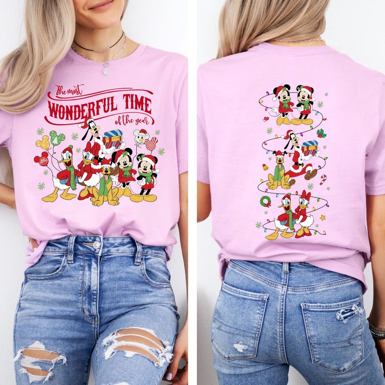May include: A light pink t-shirt featuring a festive design with Disney characters. The front of the shirt displays Mickey, Minnie, Donald, Daisy, Goofy, and Pluto in holiday attire, with the text "The most WONDERFUL TIME of the year". The back has a vertical design of the characters.