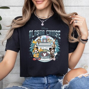 Pu&ograve; includere: T-shirt nero con la scritta "Disney Alaska Cruise" e illustrazioni di Topolino, Minnie, Paperino, Pippo e Paperina su una nave da crociera. &Egrave; presente anche l'anno "2025". La maglietta ha un girocollo.