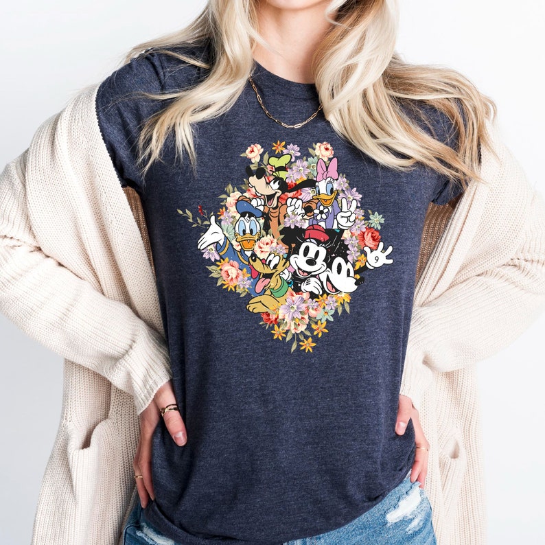 May include: A dark heather grey t-shirt with a colorful graphic of Mickey Mouse, Minnie Mouse, Donald Duck, Goofy, and Pluto surrounded by flowers.