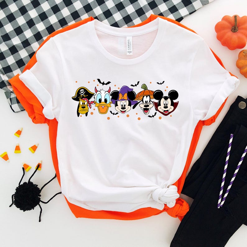 Op de afbeelding: Wit T-shirt met een afbeelding van Mickey Mouse, Minnie Mouse, Donald Duck, Goofy en Pluto verkleed in Halloween-kostuums. De personages staan in een rij met vleermuizen en pompoenen op de achtergrond.
