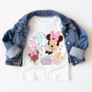 May include: White t-shirt with a cartoon image of Minnie Mouse with balloons, ice cream, and a ticket that says "Magic".
