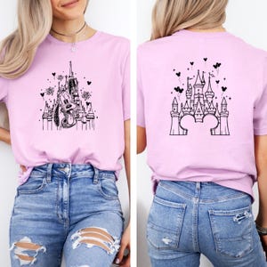 Puede incluir: Camiseta rosa claro con un dise&ntilde;o en blanco y negro de un castillo y Pluto. La parte trasera de la camiseta tambi&eacute;n presenta un dise&ntilde;o de castillo. La camiseta se combina con vaqueros azules.