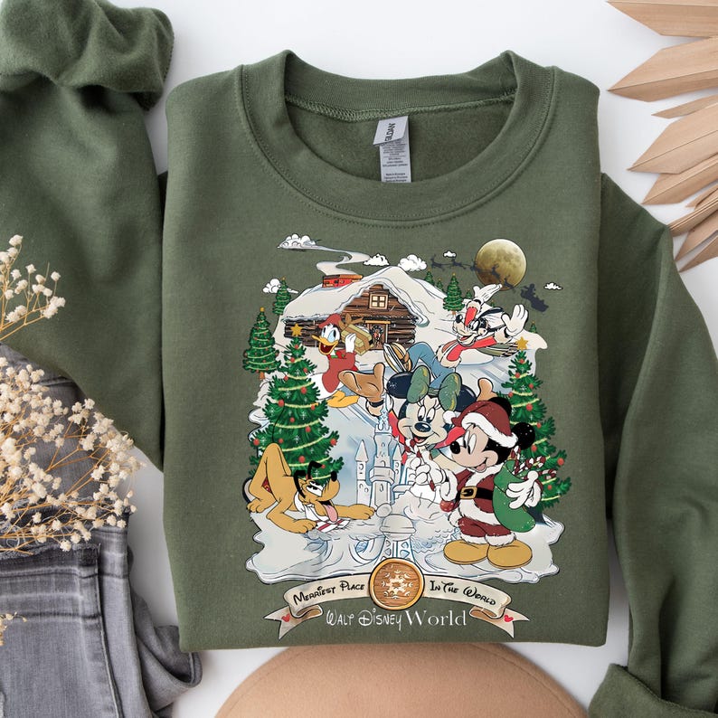 Pu&ograve; includere: Felpa verde con un design a tema natalizio con Topolino, Minnie Mouse, Paperino, Pippo e Pluto. Il design include una baita, un albero di Natale e il testo "Happiest Place on Earth, Walt Disney World".