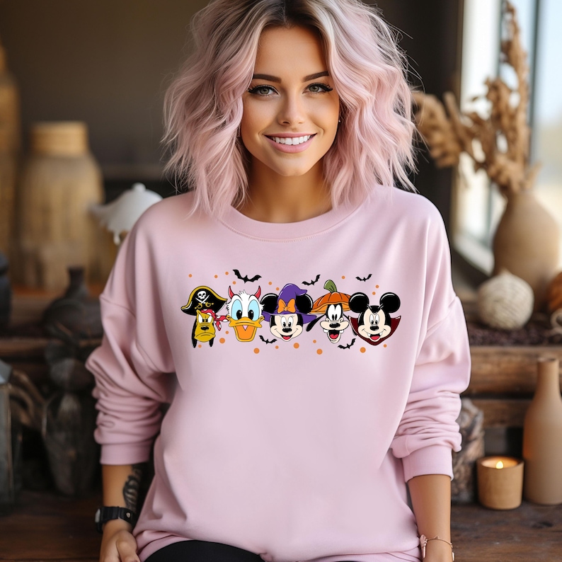 Op de afbeelding: Roze sweatshirt met een grafische print van Mickey Mouse, Minnie Mouse, Donald Duck, Goofy en Pluto in Halloween-kostuums. De personages zijn in een rij gerangschikt en hebben vleermuizen die boven hen vliegen.