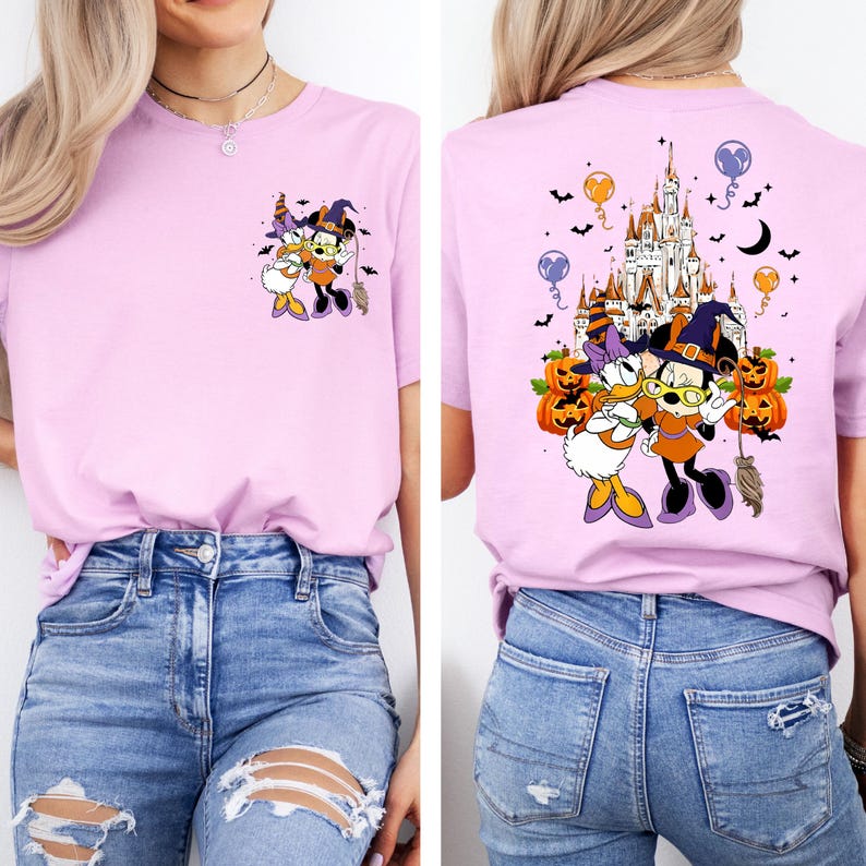 May include: A light purple t-shirt featuring a Halloween-themed graphic of Minnie Mouse and Daisy Duck in witch costumes. The back of the shirt shows a castle, pumpkins, and bats.