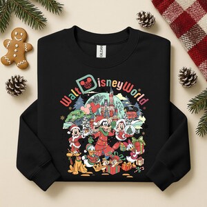 May include: Black sweatshirt featuring a colorful graphic of Disney characters in a winter scene. The design includes Mickey Mouse, Minnie Mouse, Donald Duck, and Goofy, with the words "Walt Disney World" in a festive font. The sweatshirt has a crew neck.
