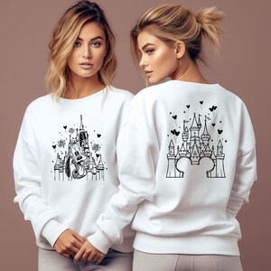Puede incluir: Sudaderas blancas con dise&ntilde;os gr&aacute;ficos negros. Una sudadera presenta un castillo con Pluto, fuegos artificiales e iconos de Mickey Mouse. La otra tiene un dise&ntilde;o de castillo con orejas de Mickey Mouse y globos en forma de coraz&oacute;n.