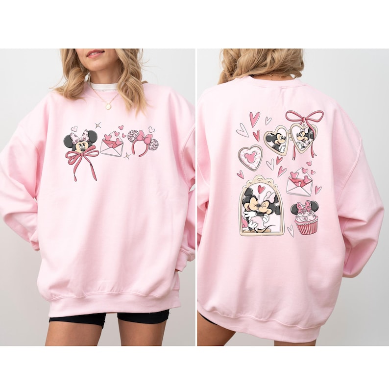 May include: Pink sweatshirt featuring Minnie Mouse-themed graphics. The front displays Minnie with a bow, hearts, and bow-shaped headbands. The back showcases Minnie in heart-shaped frames, a cupcake, and an envelope with hearts. A cozy, casual top.