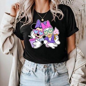 Pode incluir: Camiseta preta com uma estampa gr&aacute;fica de Mickey Mouse e Daisy Duck usando &oacute;culos de sol em forma de cora&ccedil;&atilde;o. Mickey est&aacute; segurando uma bebida rosa e Daisy est&aacute; segurando um cone de sorvete.