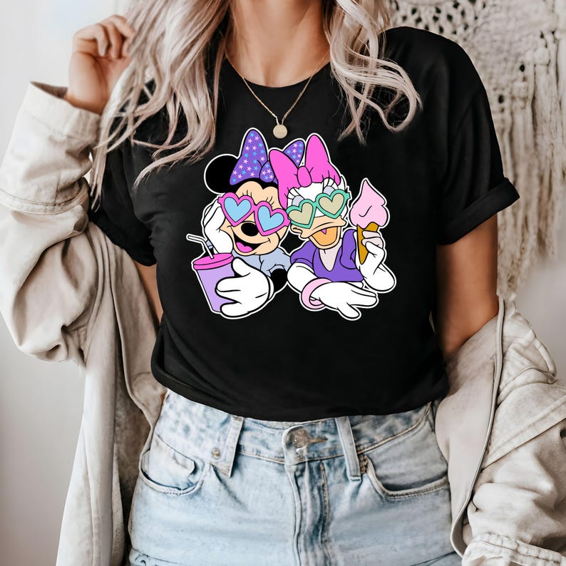 Pode incluir: Camiseta preta com uma estampa gr&aacute;fica de Mickey Mouse e Daisy Duck usando &oacute;culos de sol em forma de cora&ccedil;&atilde;o. Mickey est&aacute; segurando uma bebida rosa e Daisy est&aacute; segurando um cone de sorvete.