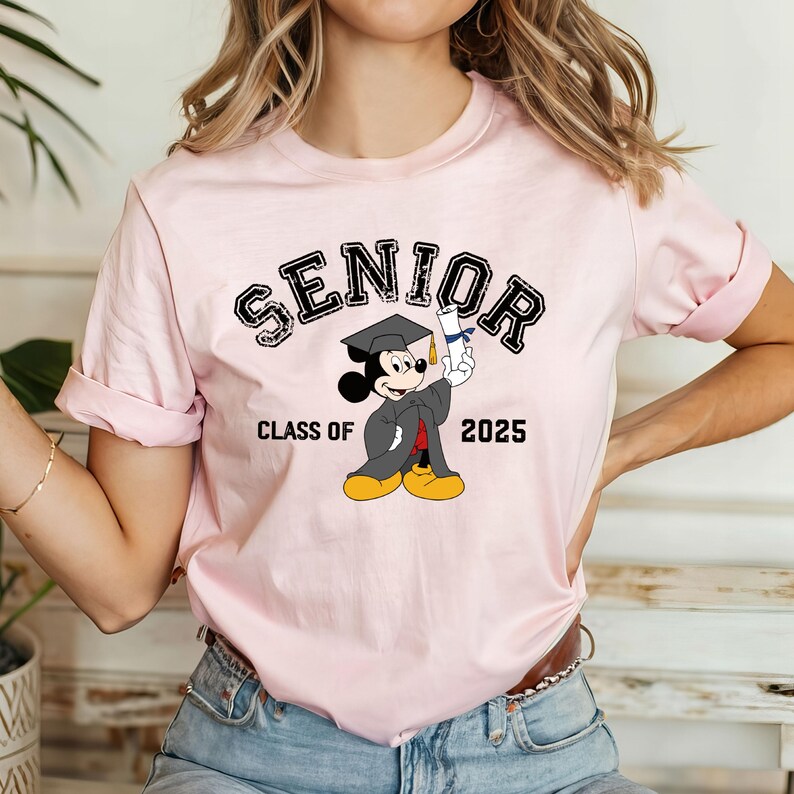 Op de afbeelding: Roze T-shirt met een zwart-witte afbeelding van Mickey Mouse die een afstudeerpet draagt en een diploma vasthoudt. De tekst "Senior Class of 2025" staat op het shirt gedrukt.