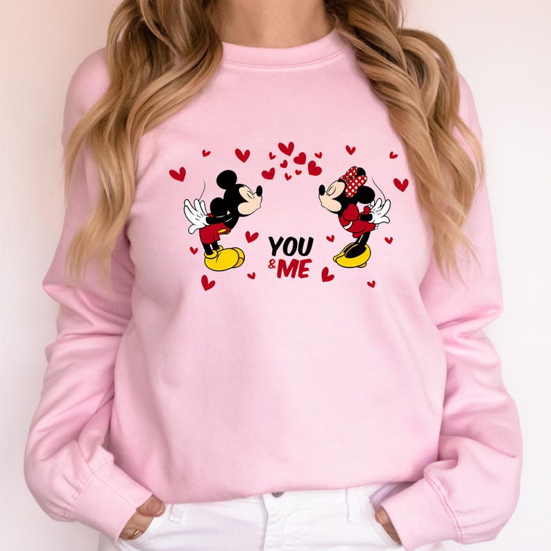 May include: Pink sweatshirt with a graphic of Mickey Mouse and Minnie Mouse kissing. The graphic includes red hearts and the text "YOU & ME".