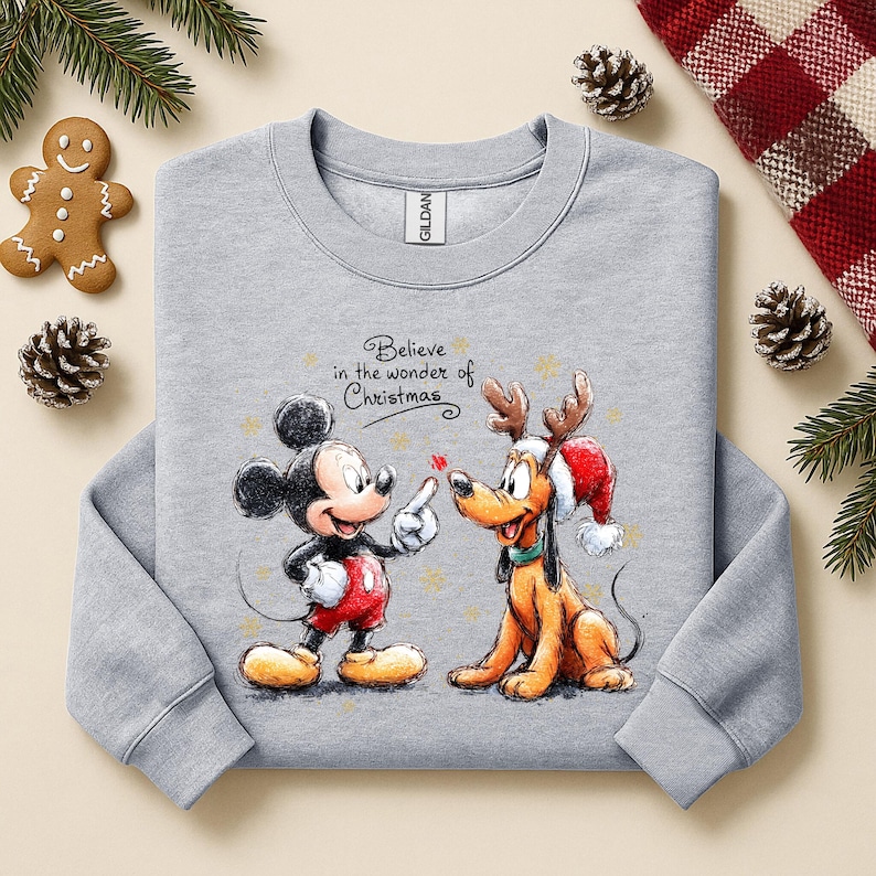 May include: A light gray sweatshirt featuring Mickey Mouse and Pluto with Christmas-themed graphics. Mickey is pointing at Pluto, who is wearing a Santa hat and reindeer antlers. The text "Believe in the wonder of Christmas" is above the characters.