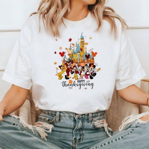 May include: White t-shirt with a colorful graphic of Mickey Mouse and friends in front of a castle with the text "Happy Thanksgiving".