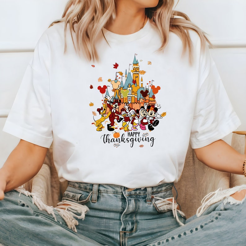 May include: White t-shirt with a colorful graphic of Mickey Mouse and friends in front of a castle with the text "Happy Thanksgiving".