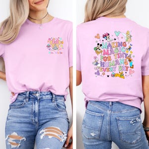 May include: A light pink t-shirt featuring a Minnie Mouse design with the text "Mrs. White" on the front. The back of the shirt has a colorful graphic with Disney characters and the phrase "Making Magic for Tiny Humans Every Day."