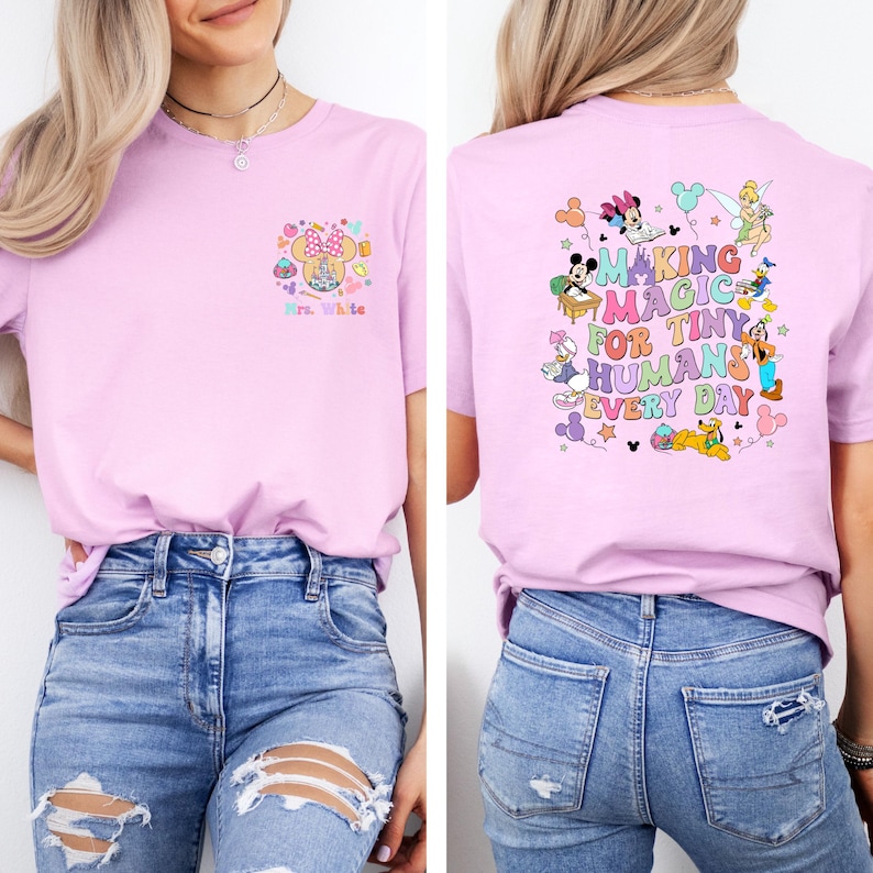 May include: A light pink t-shirt featuring a Minnie Mouse design with the text "Mrs. White" on the front. The back of the shirt has a colorful graphic with Disney characters and the phrase "Making Magic for Tiny Humans Every Day."