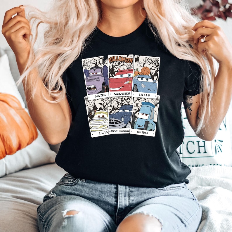 May include: Black t-shirt with a graphic of the Cars characters dressed up for Halloween. The characters include Mater, McQueen, Sally, Luigi, Doc Hudson, and Guido. The text "Halloween" is at the top of the graphic.