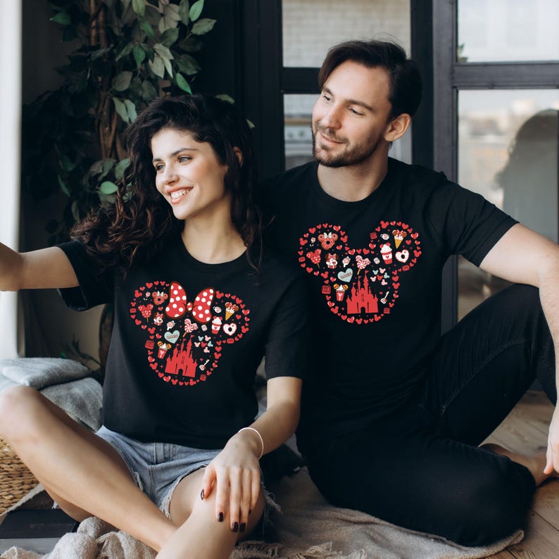 May include: A couple wearing black t-shirts with a red Mickey Mouse head design. The design is made up of various Disney-themed icons, including hearts, castles, and Mickey Mouse ears.
