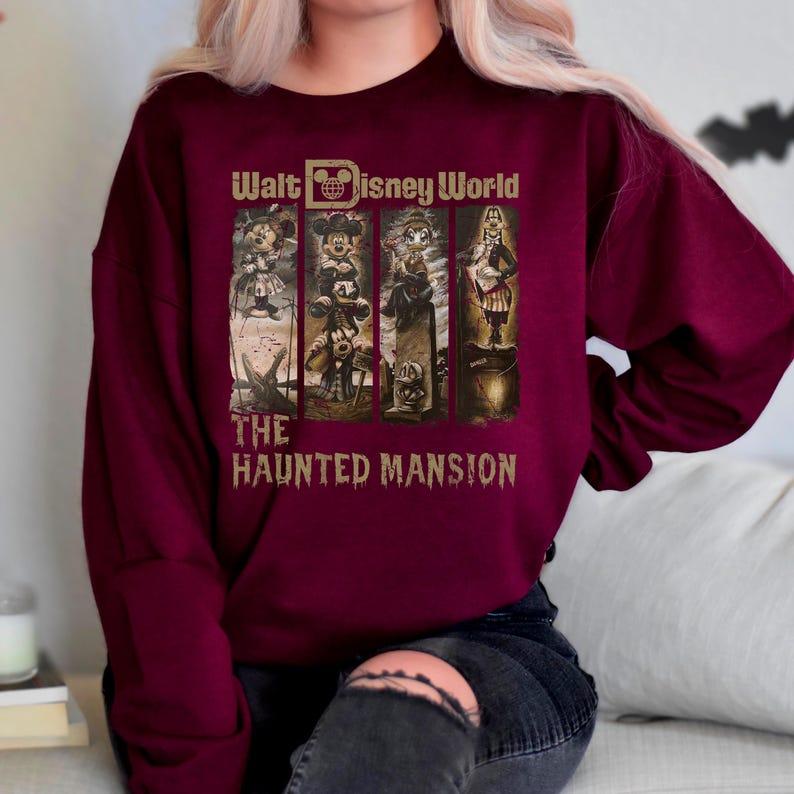 May include: A maroon sweatshirt featuring a graphic print of Mickey Mouse and other characters from the Haunted Mansion ride at Walt Disney World. The text "Walt Disney World" and "The Haunted Mansion" is printed on the sweatshirt.