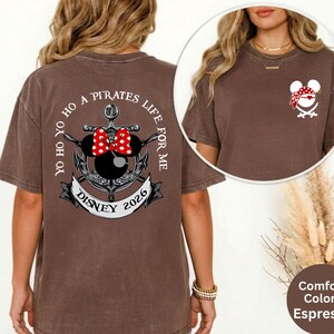 May include: Espresso-colored t-shirt with a graphic on the back featuring an anchor, Minnie Mouse ears with a red bow, and the text "Yo Ho Ho A Pirates Life For Me Disney 2026." A smaller graphic of a pirate Mickey Mouse is on the front.