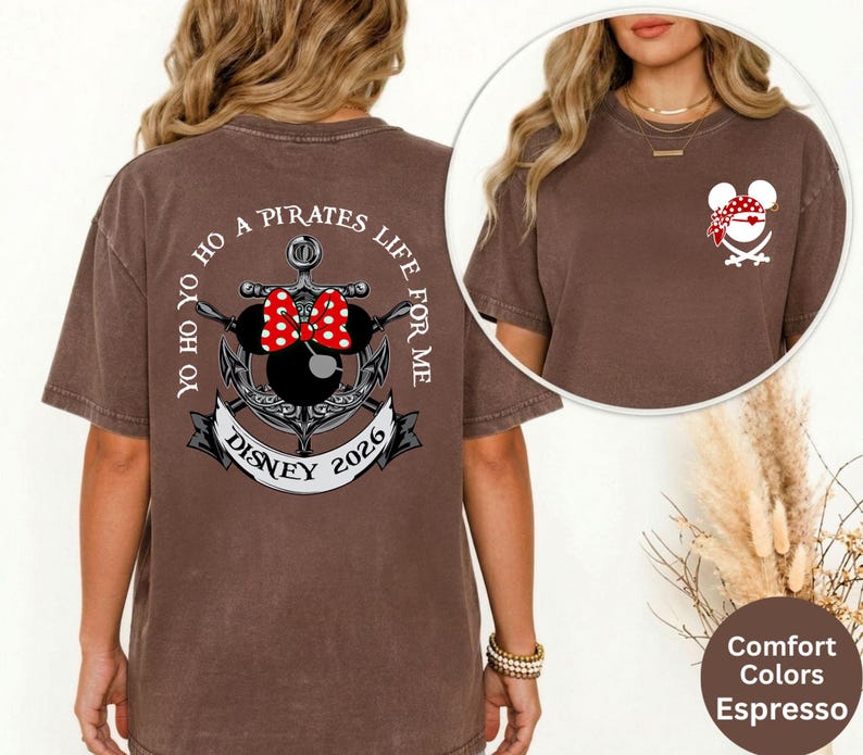 May include: Espresso-colored t-shirt with a graphic on the back featuring an anchor, Minnie Mouse ears with a red bow, and the text "Yo Ho Ho A Pirates Life For Me Disney 2026." A smaller graphic of a pirate Mickey Mouse is on the front.