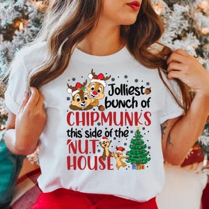 May include: White t-shirt with a Christmas-themed design featuring three cartoon chipmunks, a Christmas tree, and the text "Jolliest bunch of Chipmunks this side of the Nut House".
