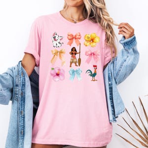 Pu&ograve; includere: Maglietta rosa con una variet&agrave; di immagini di cartoni animati colorati, tra cui un maiale, una donna con una pagaia, un gallo, un fiore e fiocchi.