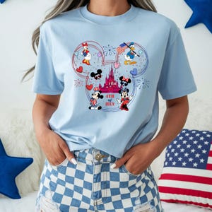 Peut inclure: T-shirt bleu clair avec un motif patriotique mettant en sc&egrave;ne des personnages Disney. Le motif comprend Mickey et Minnie Mouse, Donald Duck et Daisy Duck, ainsi qu'un ch&acirc;teau et le texte "4th of July". Le t-shirt a un col rond et des manches courtes.
