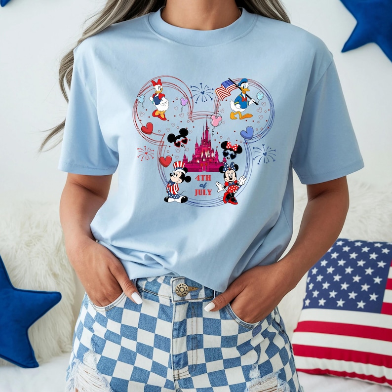 Peut inclure: T-shirt bleu clair avec un motif patriotique mettant en sc&egrave;ne des personnages Disney. Le motif comprend Mickey et Minnie Mouse, Donald Duck et Daisy Duck, ainsi qu'un ch&acirc;teau et le texte "4th of July". Le t-shirt a un col rond et des manches courtes.