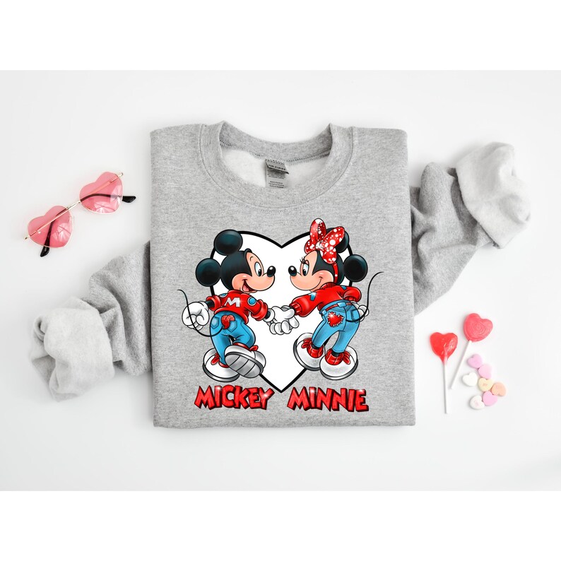 May include: Gray sweatshirt with a graphic of Mickey Mouse and Minnie Mouse holding hands inside a heart. The text "Mickey Minnie" is printed below the graphic.