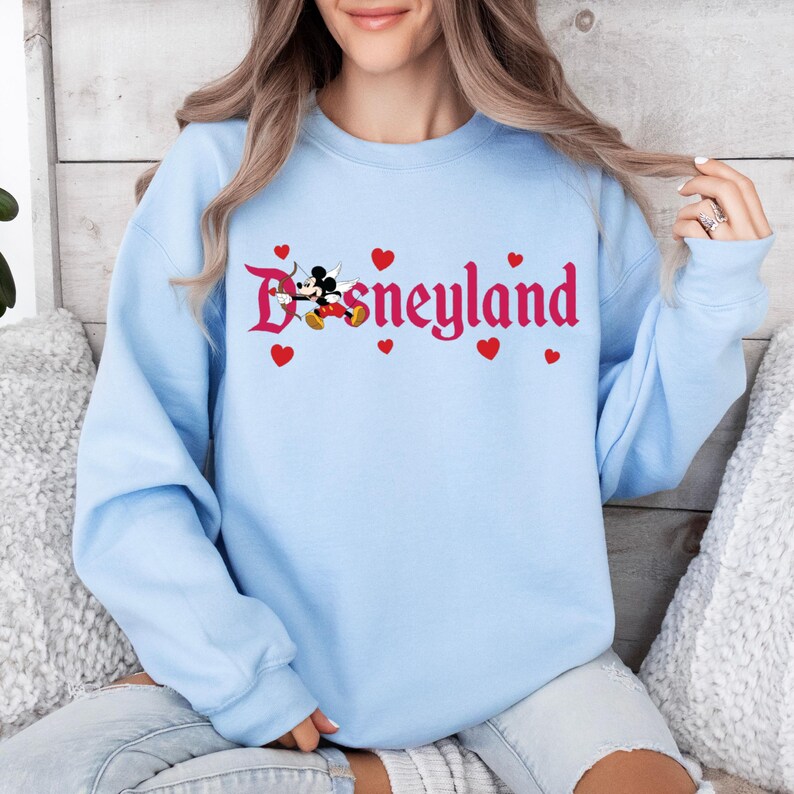 May include: Light blue sweatshirt with a red and white graphic of Mickey Mouse and Minnie Mouse with the text "Disneyland" in red.