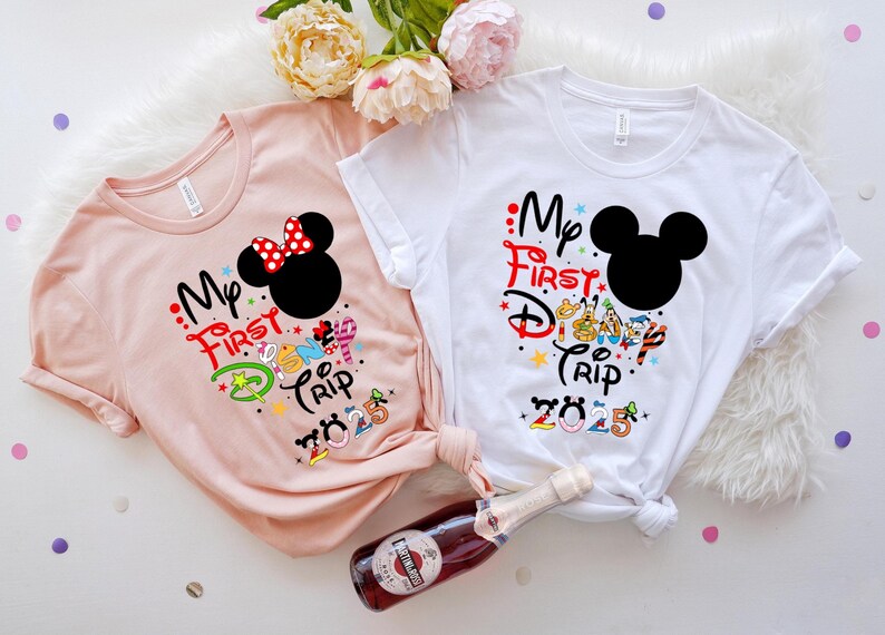 Peut inclure: Deux t-shirts &agrave; manches courtes, un rose blush et un blanc, sur le th&egrave;me de Disney. Le t-shirt rose pr&eacute;sente un design Minnie Mouse avec un n&oelig;ud rouge. Les deux chemises portent l'inscription "My First Disney Trip 2025".