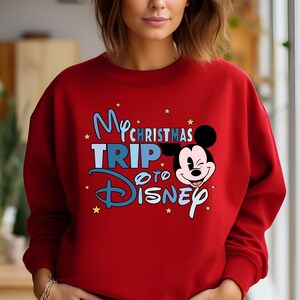 Puede incluir: Sudadera roja con un gr&aacute;fico azul y blanco que dice "My Christmas Trip to Disney" con una imagen de dibujos animados de Mickey Mouse.