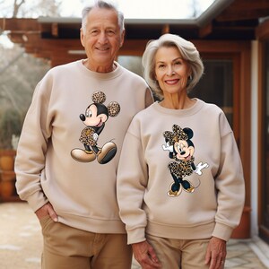 Op de afbeelding: Een stel draagt ​​passende beige sweatshirts met een cartoonafbeelding van Mickey Mouse en Minnie Mouse die kleding met luipaardprint dragen.