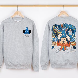 May include: Gray sweatshirt with a Mickey Mouse illustration wearing a sorcerer hat on the back. The front of the sweatshirt has a smaller Mickey Mouse sorcerer hat illustration and the word "Name" underneath.